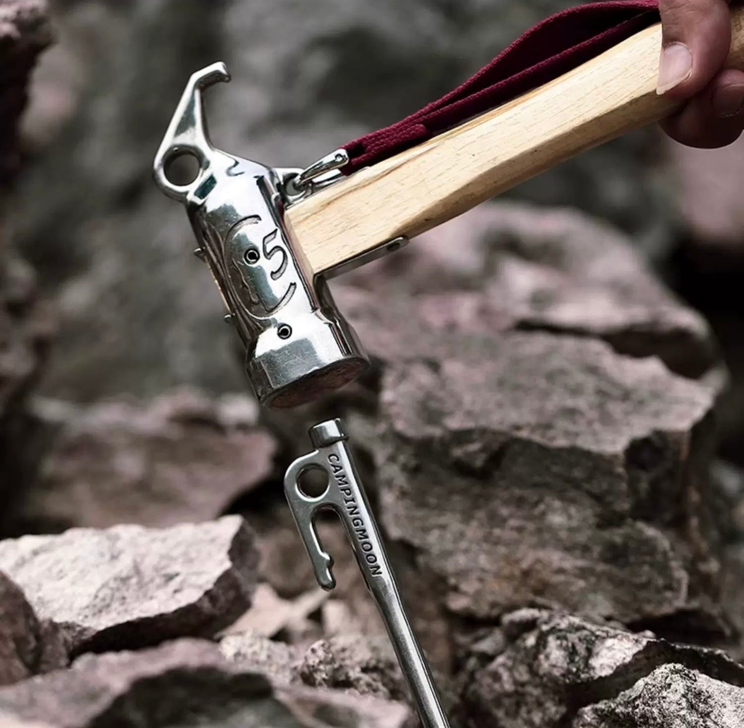 Metal hammer with wooden handle hammering the Nomadia Accessory Forged Camp Pegs against a rocky background - camping essential -tent pegs - wild camping
