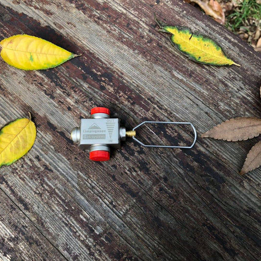 Nomadia Accessory Fuel Canister Refill Adapter. Small valve or fitting on a wooden surface with leaves around - camping gear - camping essential