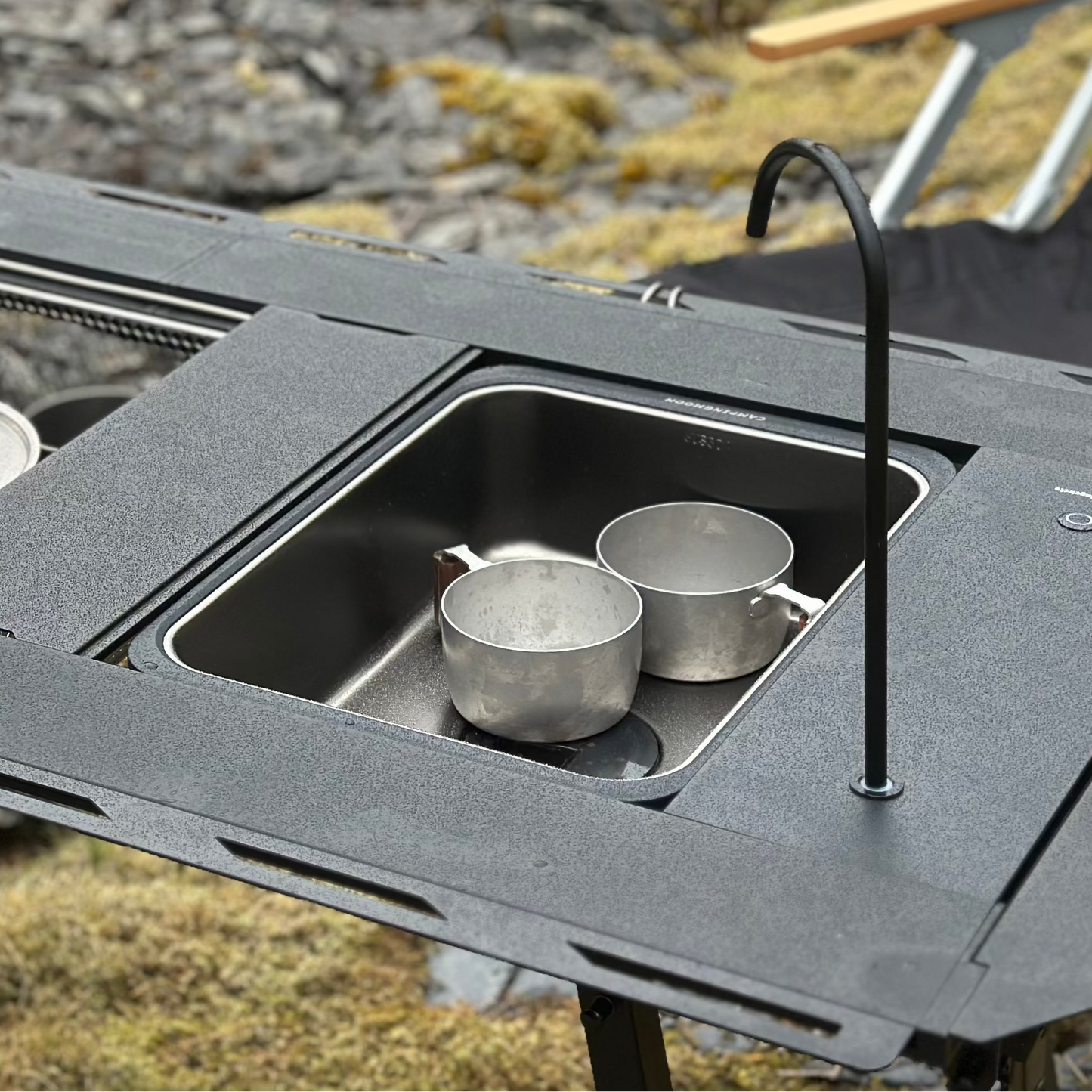 Portable outdoor modular camping table setup with Nomadia CampStation Kitchen Sink, stove set and pots on a natural background