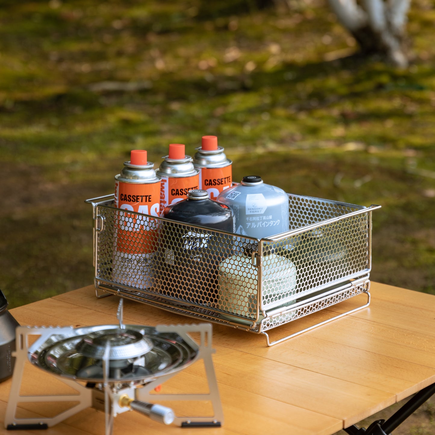 metal mesh basket with various sized gas canister on a wooden camping table outdoor - camping gear - multi purpose - glamping