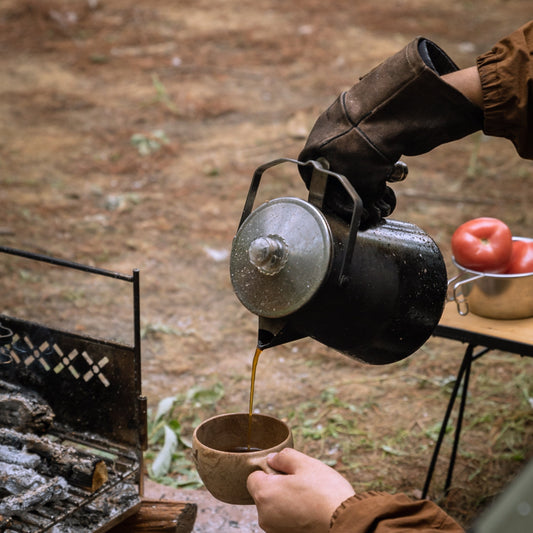 Person pouring coffee from Nomadia CampStation Stainless Steel Coffee Pot into a cup outdoors near a camping campfire - outdoor cooking - uk camping - wildcamping