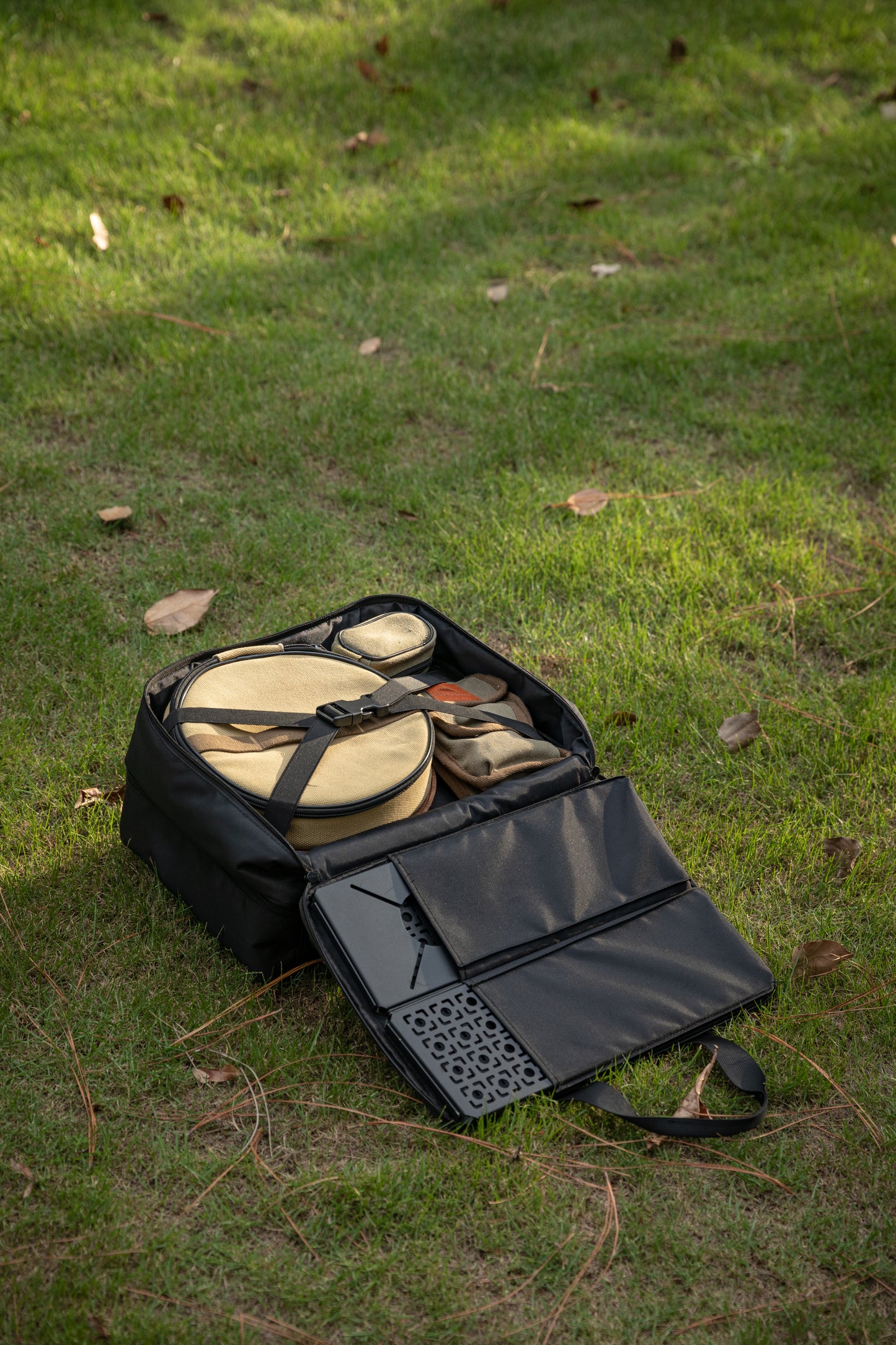 Black Nomadia CampStation Storage Bag with camping gear on a grassy ground - large storage camping bag for modular camping table