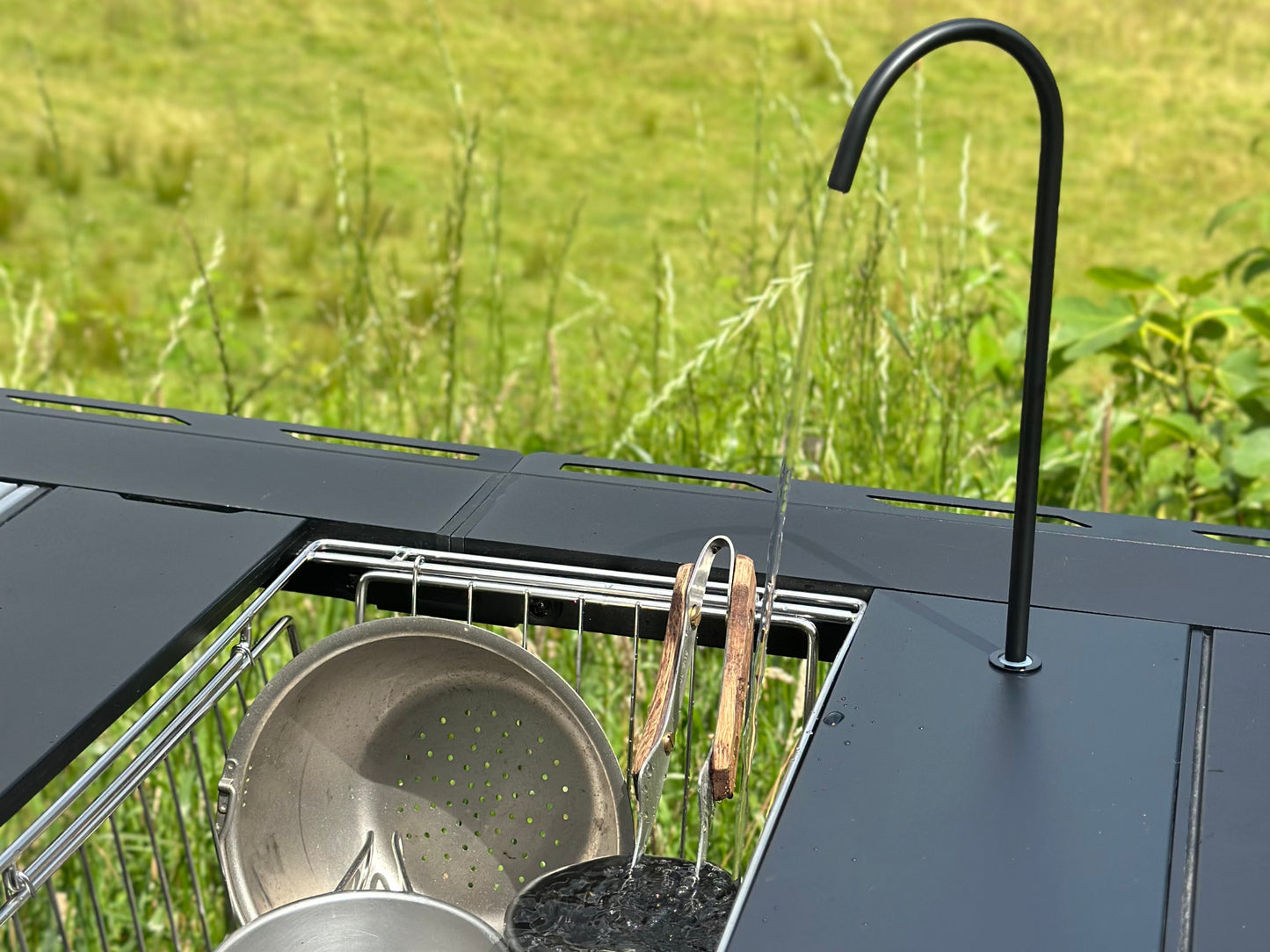 Outdoor kitchen setup with grill, pots, and Nomadia CampStation Water Dispenser on a grassy background - outdoor cooking - camping gear - glamping