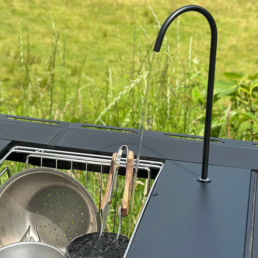 Outdoor kitchen setup with grill, pots, and Nomadia CampStation Water Dispenser on a grassy background - outdoor cooking - camping gear - glamping