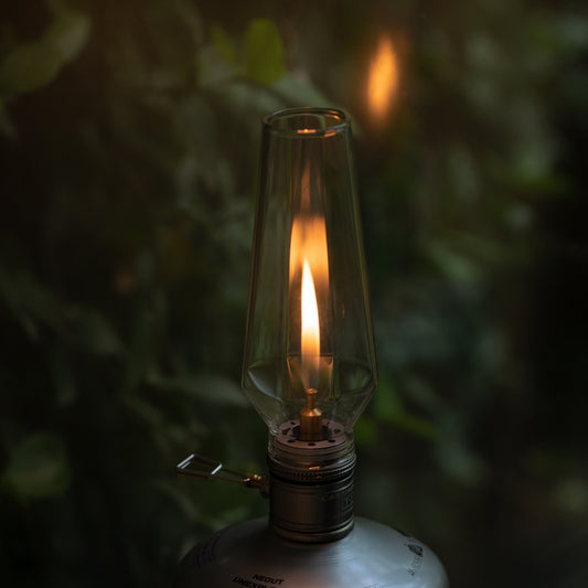 Vintage-style gas lamp with a lit wick against a dark, leafy background - wildcamping accessory - camping accessory - camping with a fire