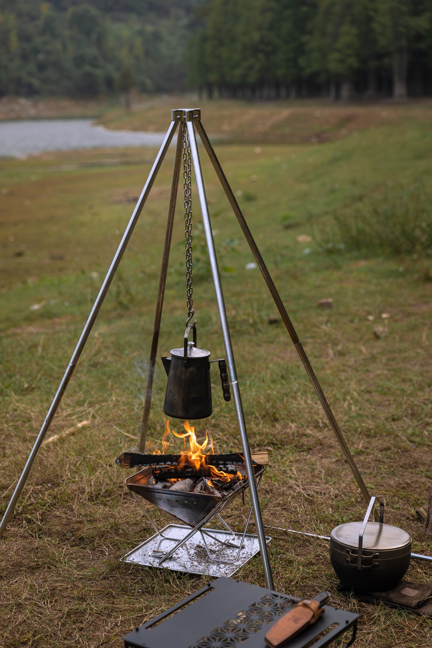 Outdoor camping setup with tripod quadripod fire pit and Nomadia Flamo Crafted Camping Kettle over a fire pit in a natural setting. camping with fire - wild camping