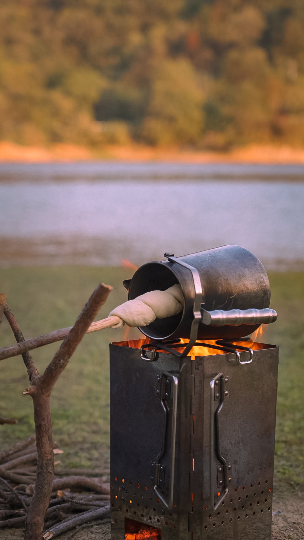 Nomadia Flamo Crafted Camping Kettle used as roasting device over a fire with bread being roasted, set against a natural background - multi-use - multi-purpose - camping with fire - wildcamping