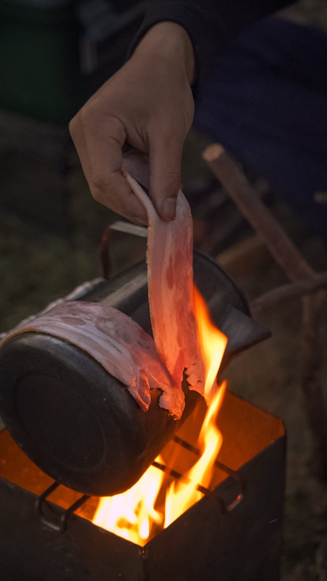 Person roasting bacons using Nomadia Flamo Crafted Camping Kettle over a campfire - camping with fire - wild camping