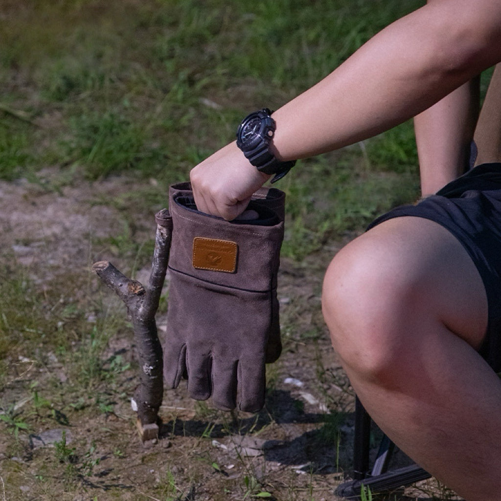 Person putting Nomadia Flamo Heavy-Duty Leather Fire Gloves to a stick in a natural setting - camping essential - camping gear -wildcamping