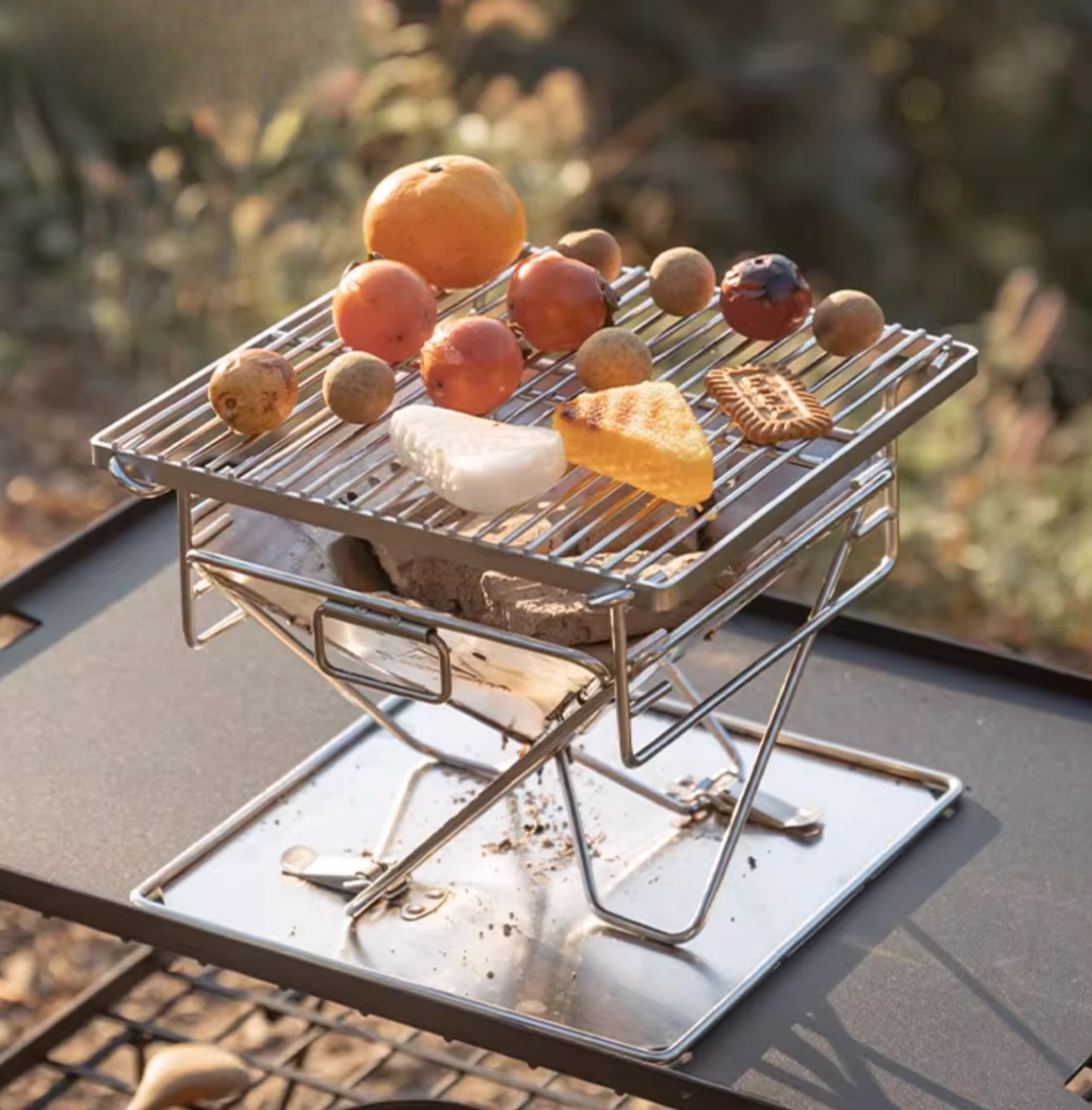 mini Nomadia's Flamo Portable Folding BBQ Grill and Fire Pit with fruits and bread on top