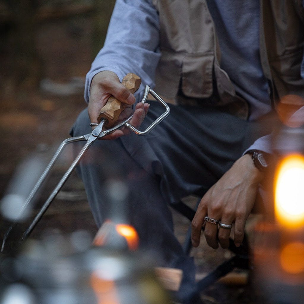 Person holding Nomadia Flamo Precision Grip Fire Tongs over a campfire - wildcamping - camping with a fire - uk camping