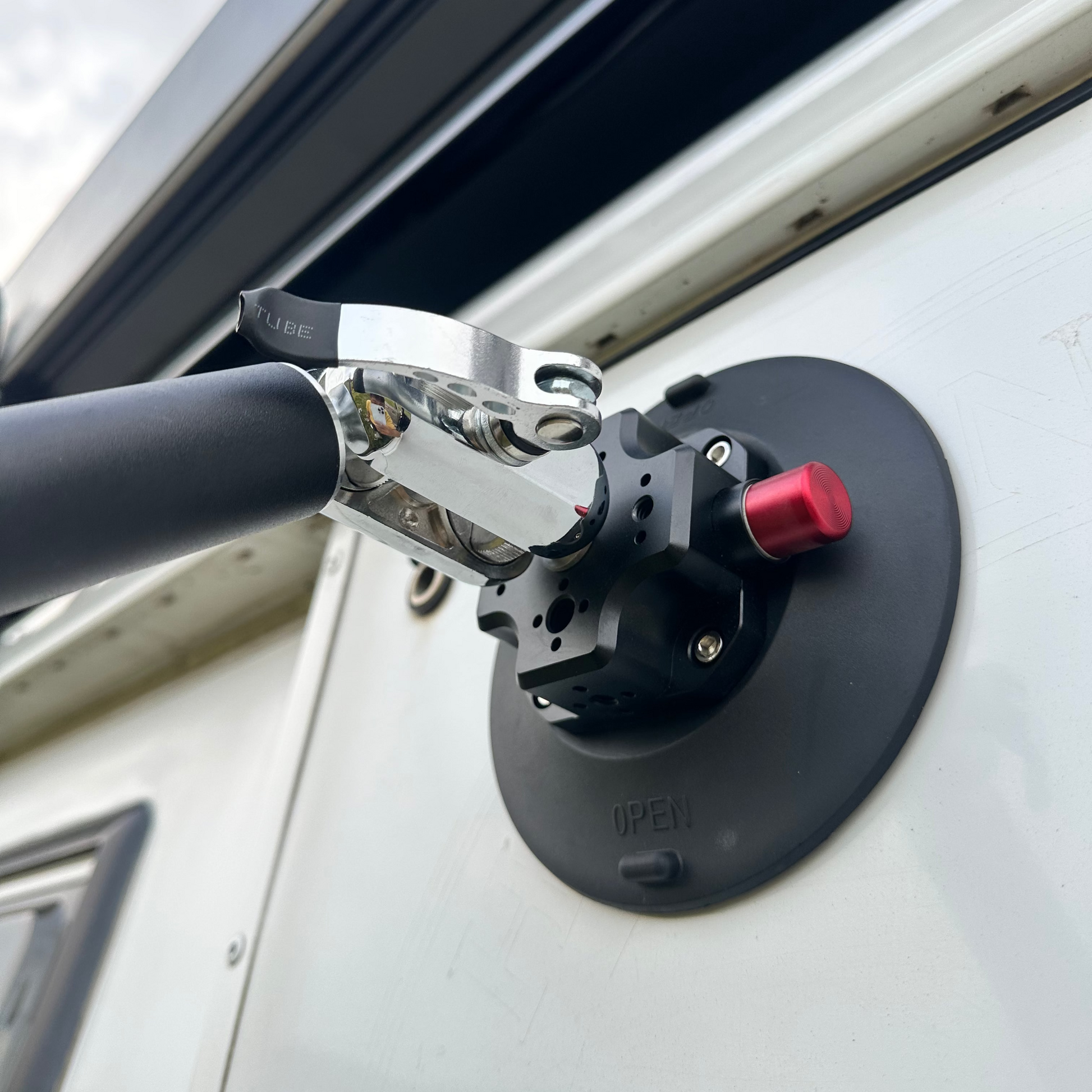 Close-up of a vehicle roof rack mount Nomadia FlexMount Suction Arm on a white van with a cloudy sky background - camping and survival -