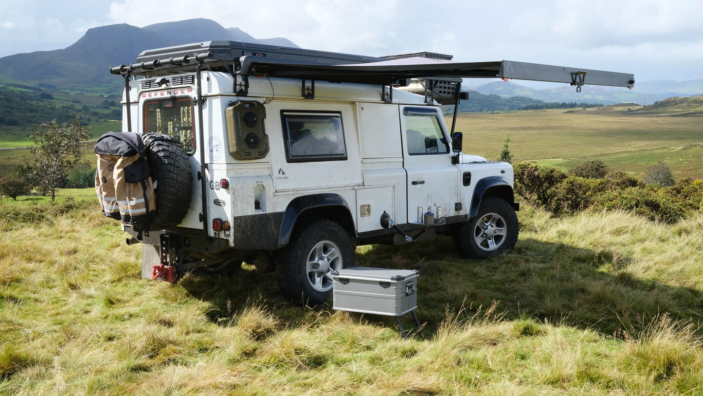 White off-road vehicle with World's fastest opening awning in a camping setup in a grassy field with mountains in the background - overlanding - wildcamping - aluminium awning - easy setup - fast setup awning