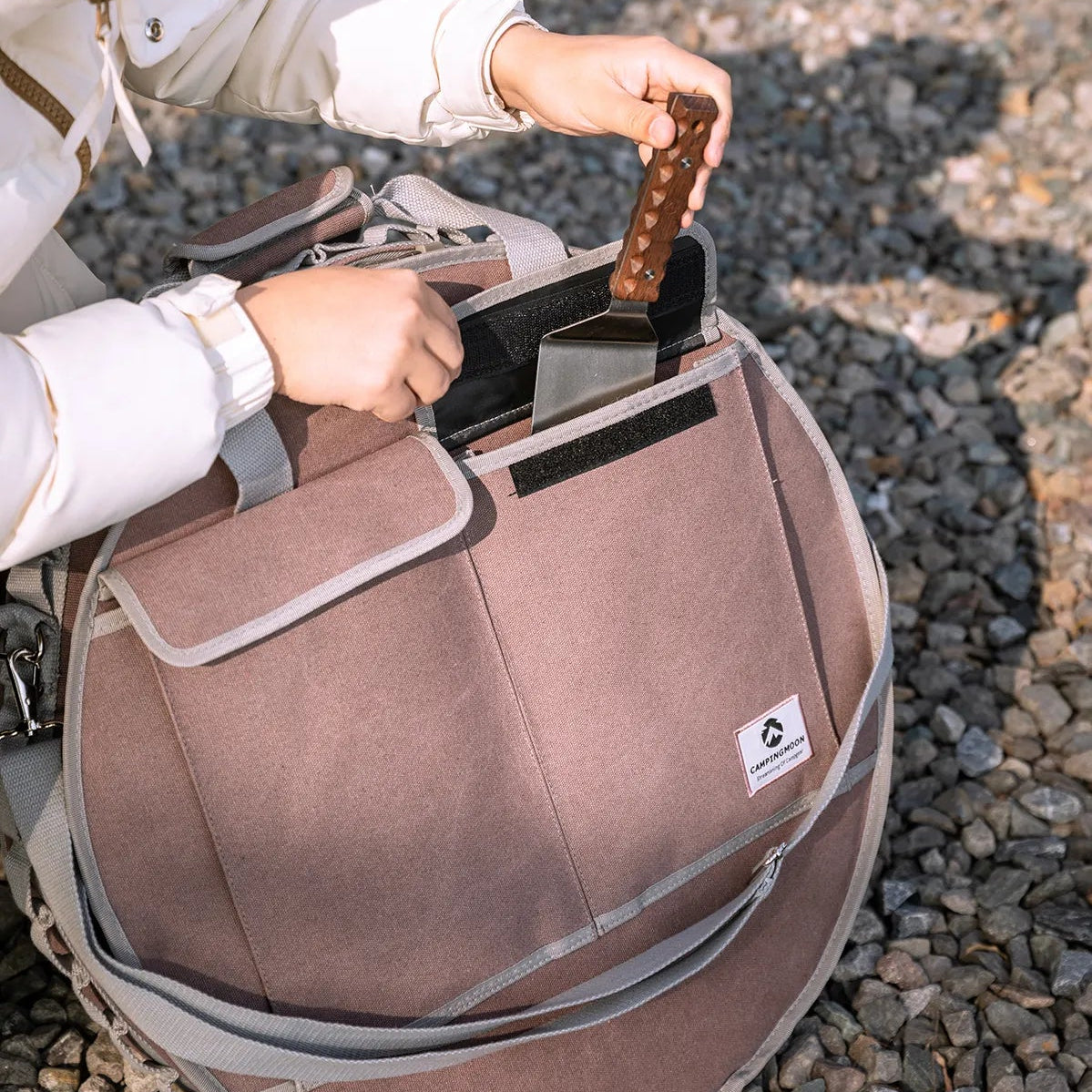 person placing cooking utensils into storage bag of Nomadia Horizon Cook portable outdoor cooking station for sharing - portable grill pan - outdoor cookware for groups - multi-function camping stove - smart storage - vanlife cooking gear - campervan kitchen setup