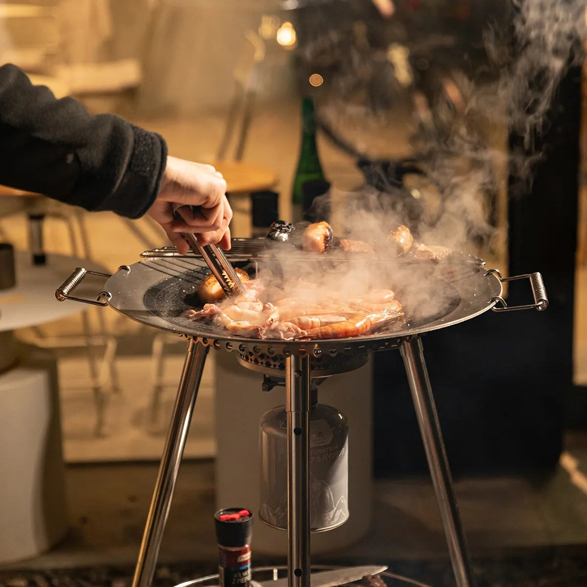 Person grilling food using Nomadia Horizon Cook portable outdoor cooking station for sharing - portable grill pan - outdoor cookware for groups - multi-function camping stove