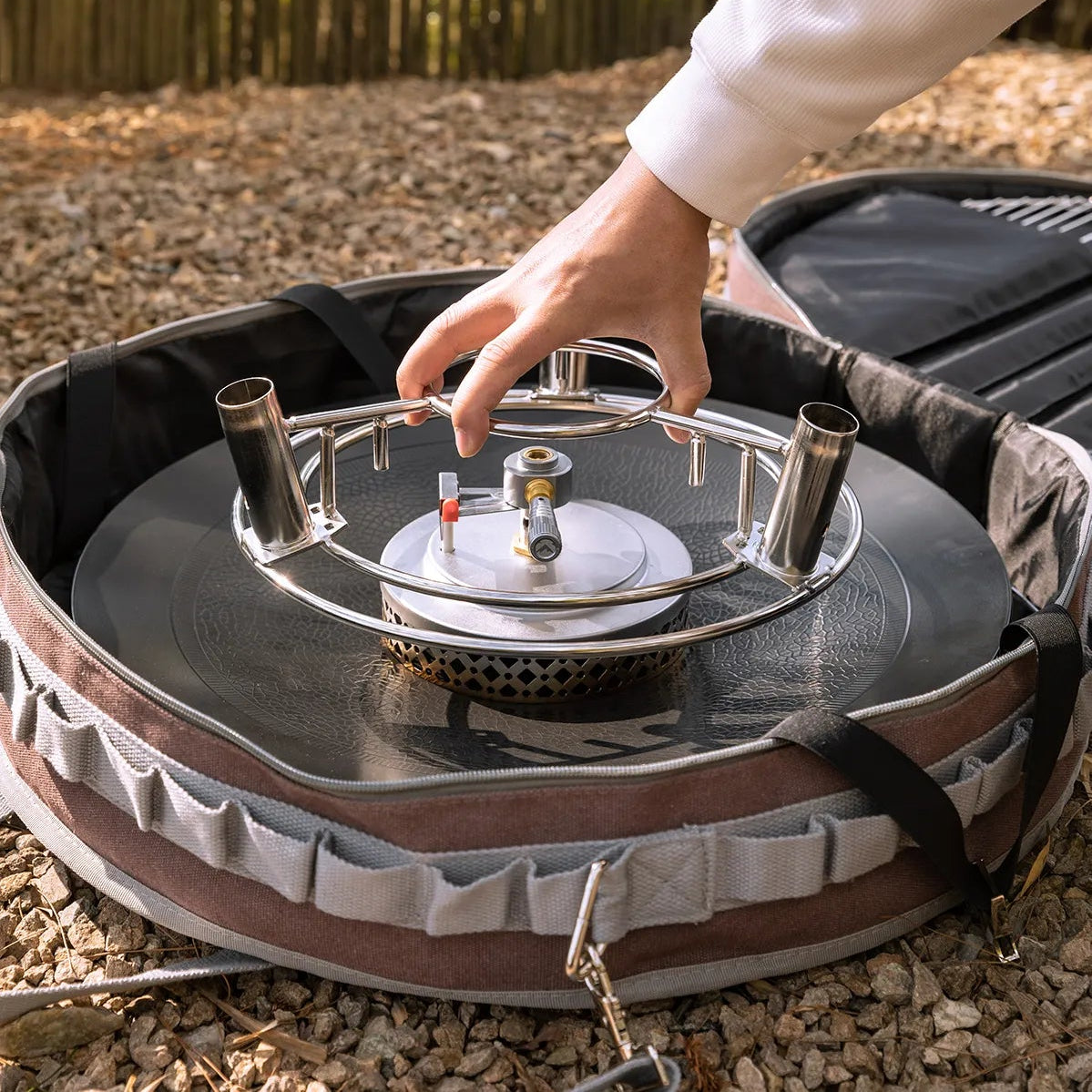 person placing Nomadia Horizon Cook portable outdoor cooking station for sharing into storage bag - portable grill pan - outdoor cookware for groups - multi-function camping stove - compact camp kitchen - smart storage
