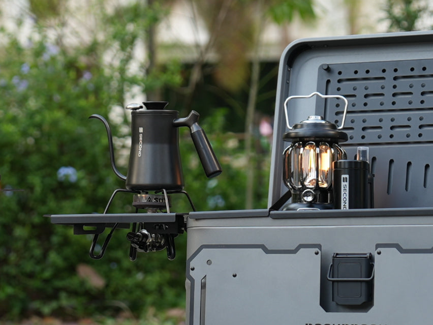 Outdoor camping setup with coffee maker and lantern on Nomadia ModoBox 2in1 camping table and storage box, surrounded by greenery - amping gear - glamping - uk camping
