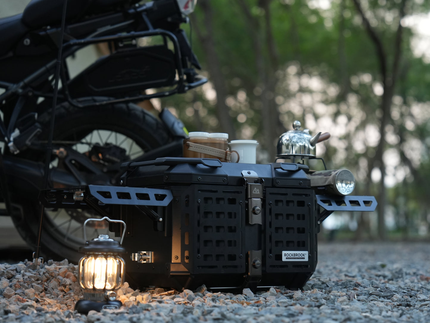 Motorcycle with Nomadia ModoBox ArmorFold 45 Motorcycle Trunk Camping Table and lanterns on a gravel surface - overlanding in uk - multi-use
