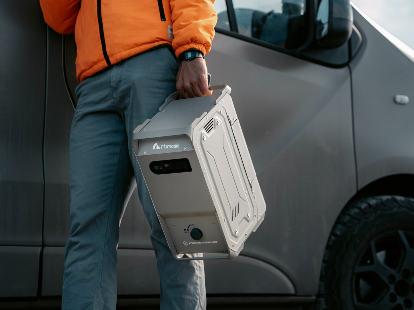 Person holding Nomadia's thermoflow - portable heated shower system next to a van