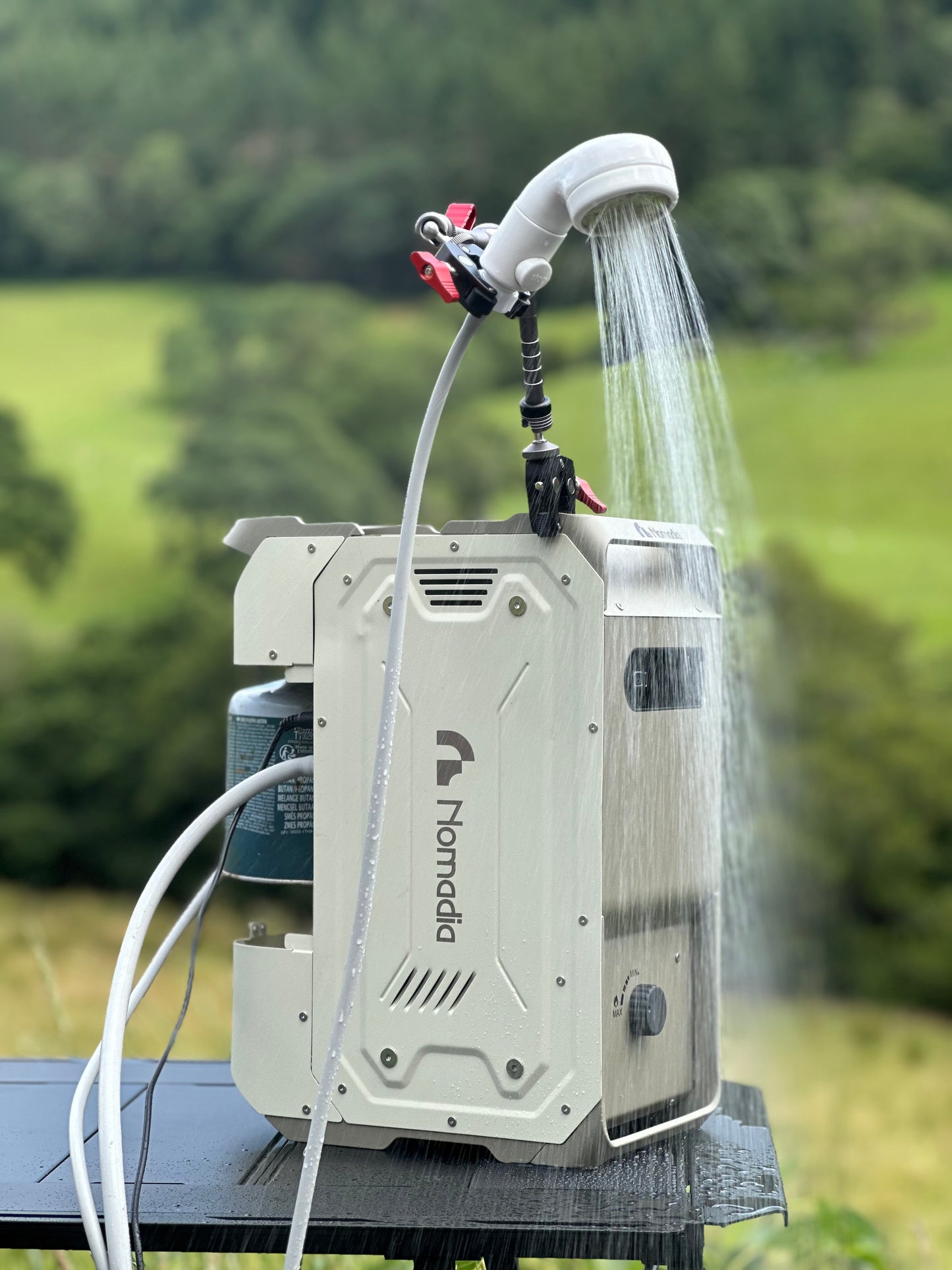 ThermoFLow - Portable heated shower system with Nomadia branding in use with running hot water in natural background