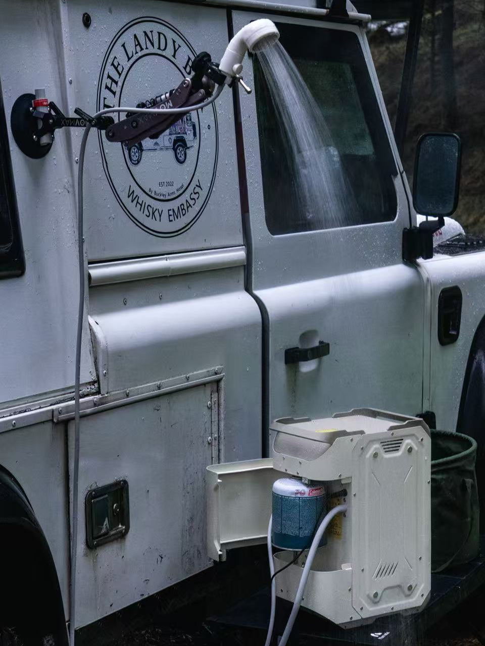 Nomadia ThermoFlow Portable Heated Shower next to a white van with a water hose attached to the side of the van for easy shower in the wild - wildcamping - uk camping - outdoor gear