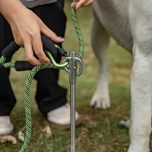 Person holding a dog leash attaching to Nomadia Accessory Fuel Canister Refill Adapter, with a dog's paw visible in the background - camping gear - camping with dog - animal friendly