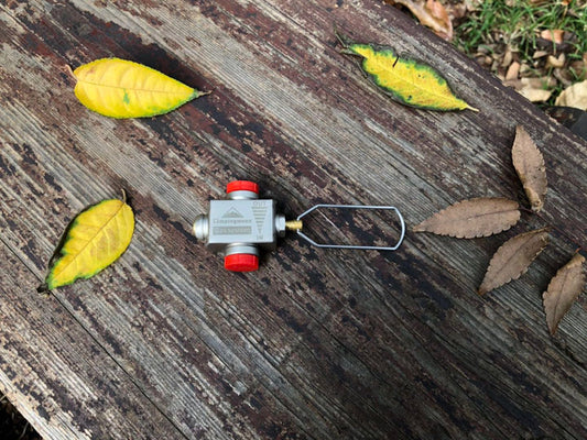 Nomadia Accessory Fuel Canister Refill Adapter. Small valve or fitting on a wooden surface with leaves around - camping gear - camping essential 