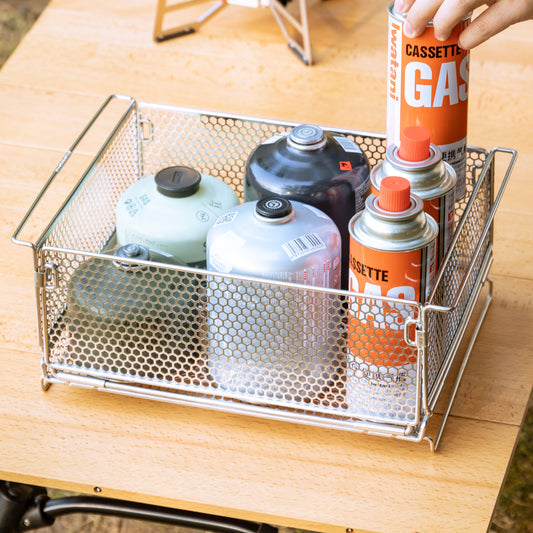 Metal mesh storage basket with canisters on a wooden surface - for camping use - outdoor gear - stainless steel