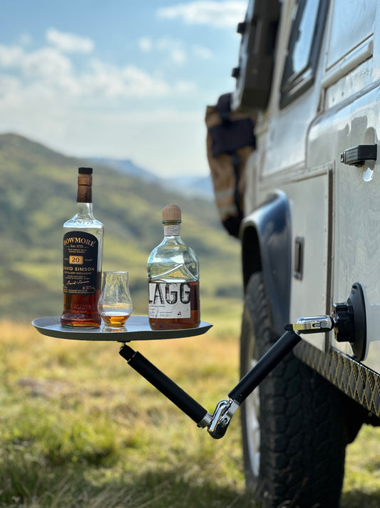 Two bottles of alcohol and a glass on a tray attached to a vehicle using Nomadia FlexMount Suction Arm with mountains in the background - camping and survival - uk camping - strong powerful and reliable