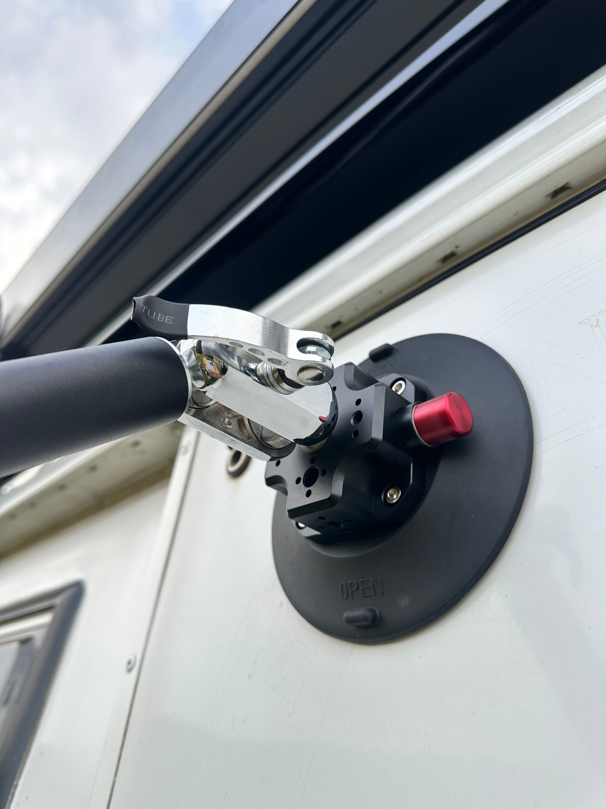 Close-up of a vehicle roof rack mount Nomadia FlexMount Suction Arm on a white van with a cloudy sky background - camping and survival - 