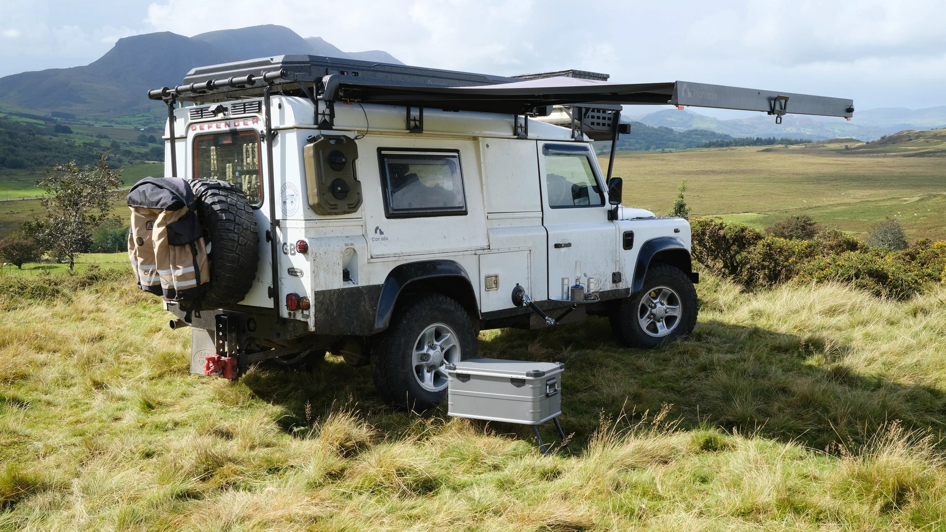 White off-road vehicle with World's fastest opening awning in a camping setup in a grassy field with mountains in the background - overlanding - wildcamping - aluminium awning - easy setup - fast setup awning