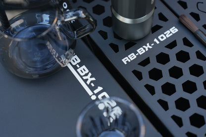 Close-up of a coffee brewing setup using Nomadia ModoBox 2in1 camping table and storage box with a glass carafe and a black metal tray