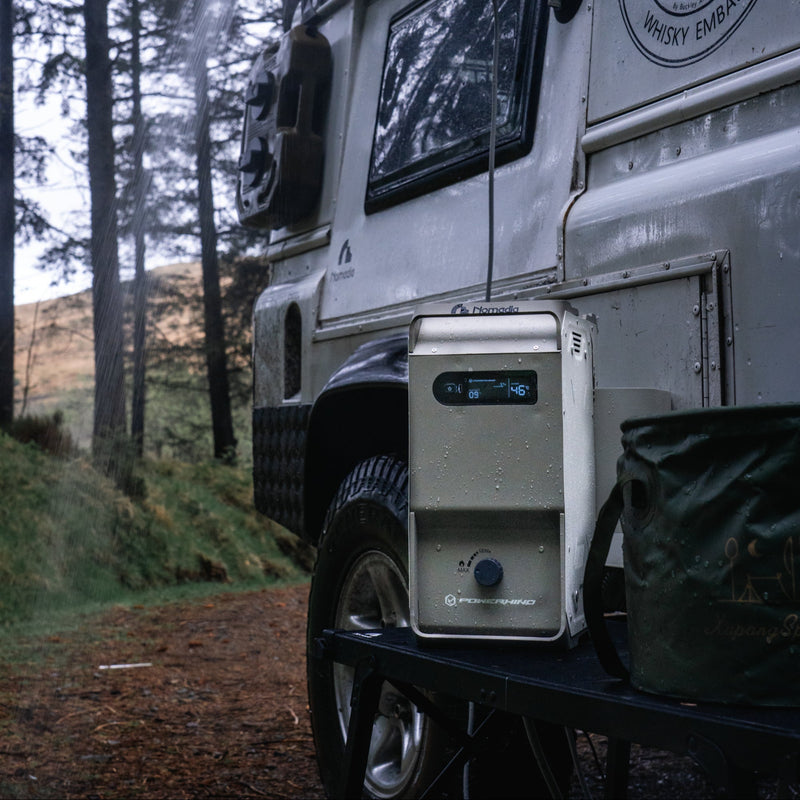 Nomadia ThermoFlow Portable Heated Shower next to a white van with a water hose attached to the van and hot water running in a forest. wildcamping - camping gear - uk camping - portable shower for camping 