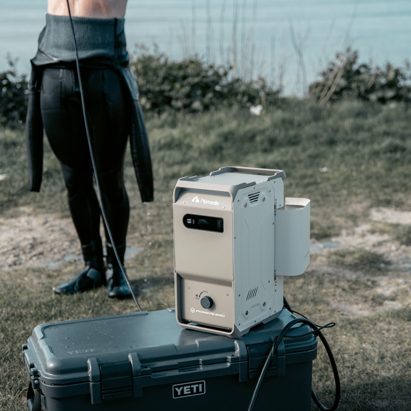 nomadia's thermoflow - a Portable heated shower system on a container outdoors. a man uses it to take a shower after surfing -camping gear - uk camping -outdoorsy - portable shower for outdoor use