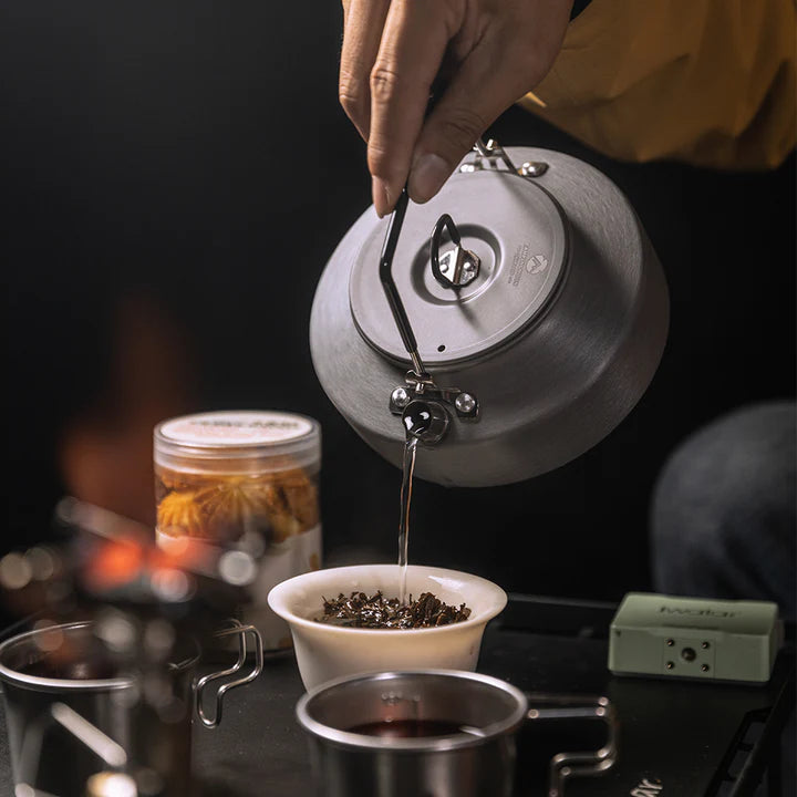 Person pouring tea from Nomadia fast boil camping kettle for gas stove into a small bowl with tea on a dark background - multiuse kettle - small camping kettle - campervan kettle 