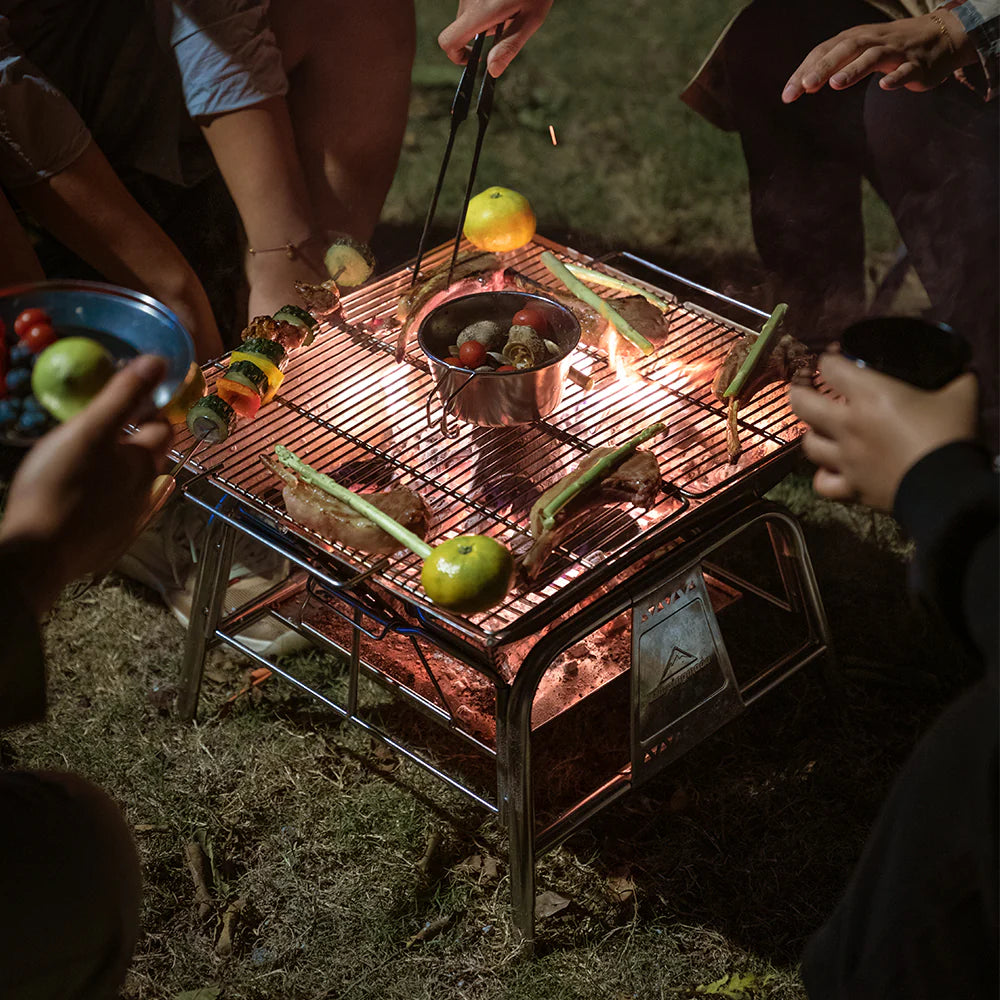 Nomadia's Flamo Portable Folding BBQ Grill and Fire Pit Stand Alone with food being cooked on a natural outdoor setting - wildcamping - camping with a fire - uk camping - fire camping
