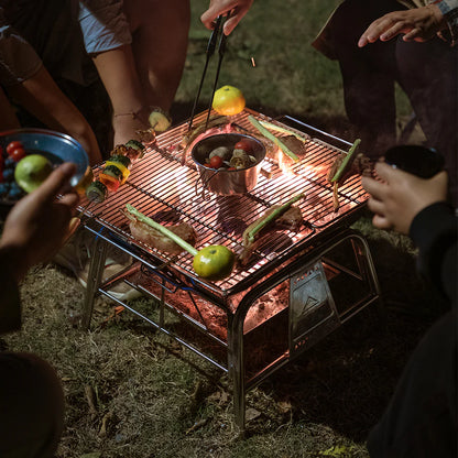 Nomadia's Flamo Portable Folding BBQ Grill and Fire Pit Stand Alone with food being cooked on a natural outdoor setting - wildcamping - camping with a fire - uk camping - fire camping