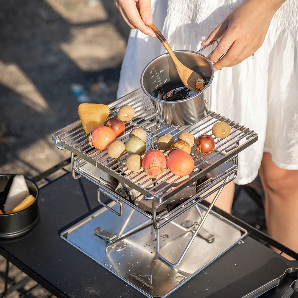 Nomadia's Flamo Portable Folding BBQ Grill and Fire Pit with food being cooked on a natural outdoor setting - wildcamping - camping with a fire - uk camping - glamping