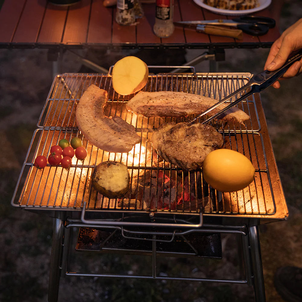 grill scene with Nomadia's Flamo Portable Folding BBQ Grill and Fire Pit standalone -  with food being cooked on a natural outdoor setting - wildcamping - camping with a fire - uk camping - outdoor grill
