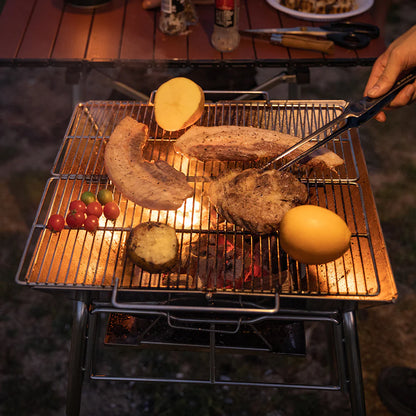 grill scene with Nomadia's Flamo Portable Folding BBQ Grill and Fire Pit standalone -  with food being cooked on a natural outdoor setting - wildcamping - camping with a fire - uk camping - outdoor grill