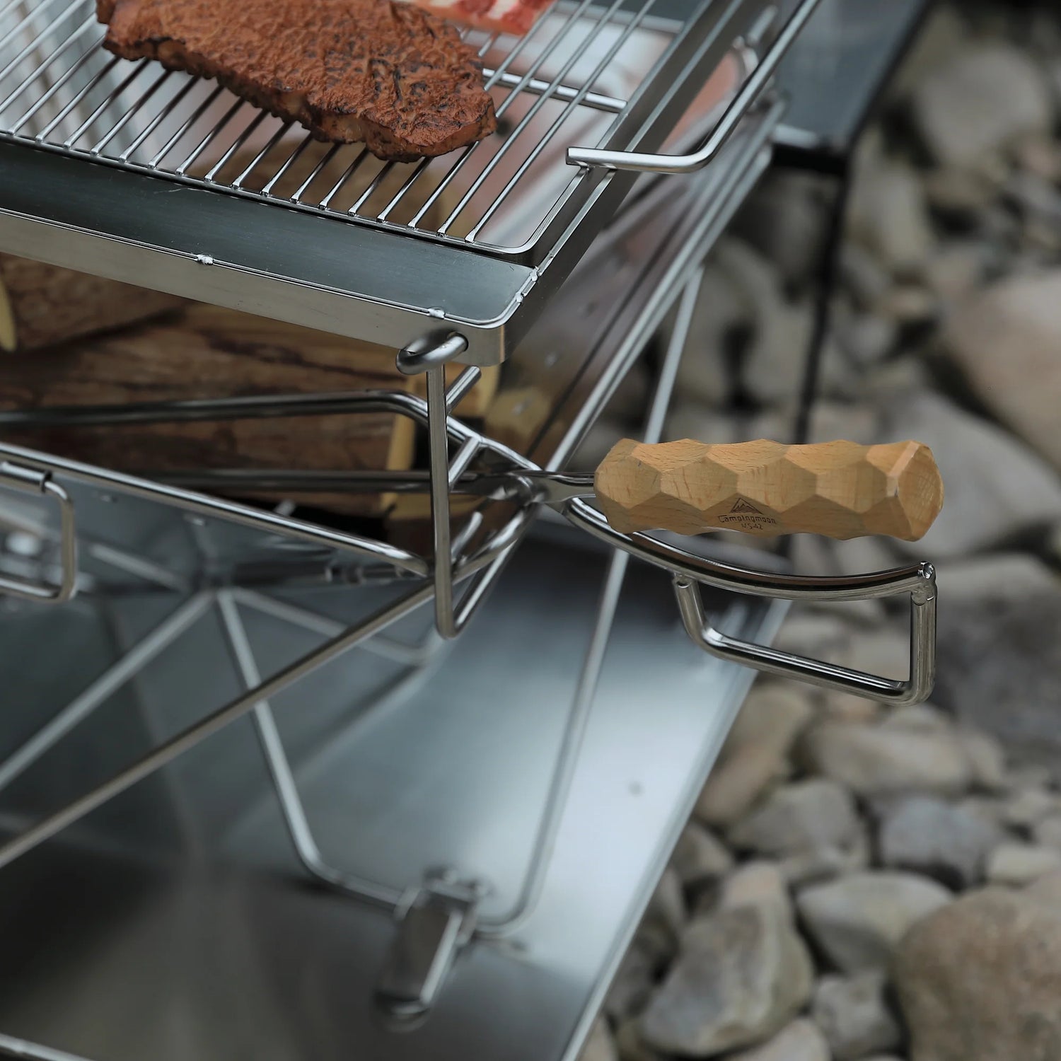 Nomadia's Flamo Portable Folding BBQ Grill and Fire Pit with food being cooked on a natural outdoor setting - wildcamping - camping with a fire - uk camping - adjustable height